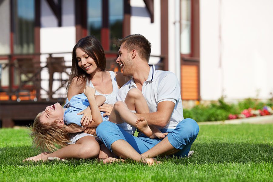 Personal Insurance - Happy Family Sitting on Grass Outside Their Home Playing Together